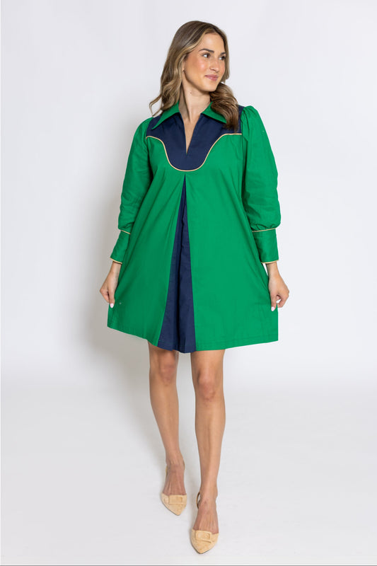 A woman modeling a green and navy blue color-blocked mini dress with long sleeves and a notched collar, standing against a light gray studio background.