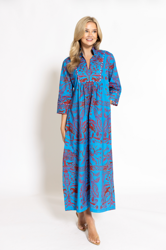 A woman modeling a long-sleeve maxi dress with a vibrant blue and red abstract pattern, standing against a plain white studio background.